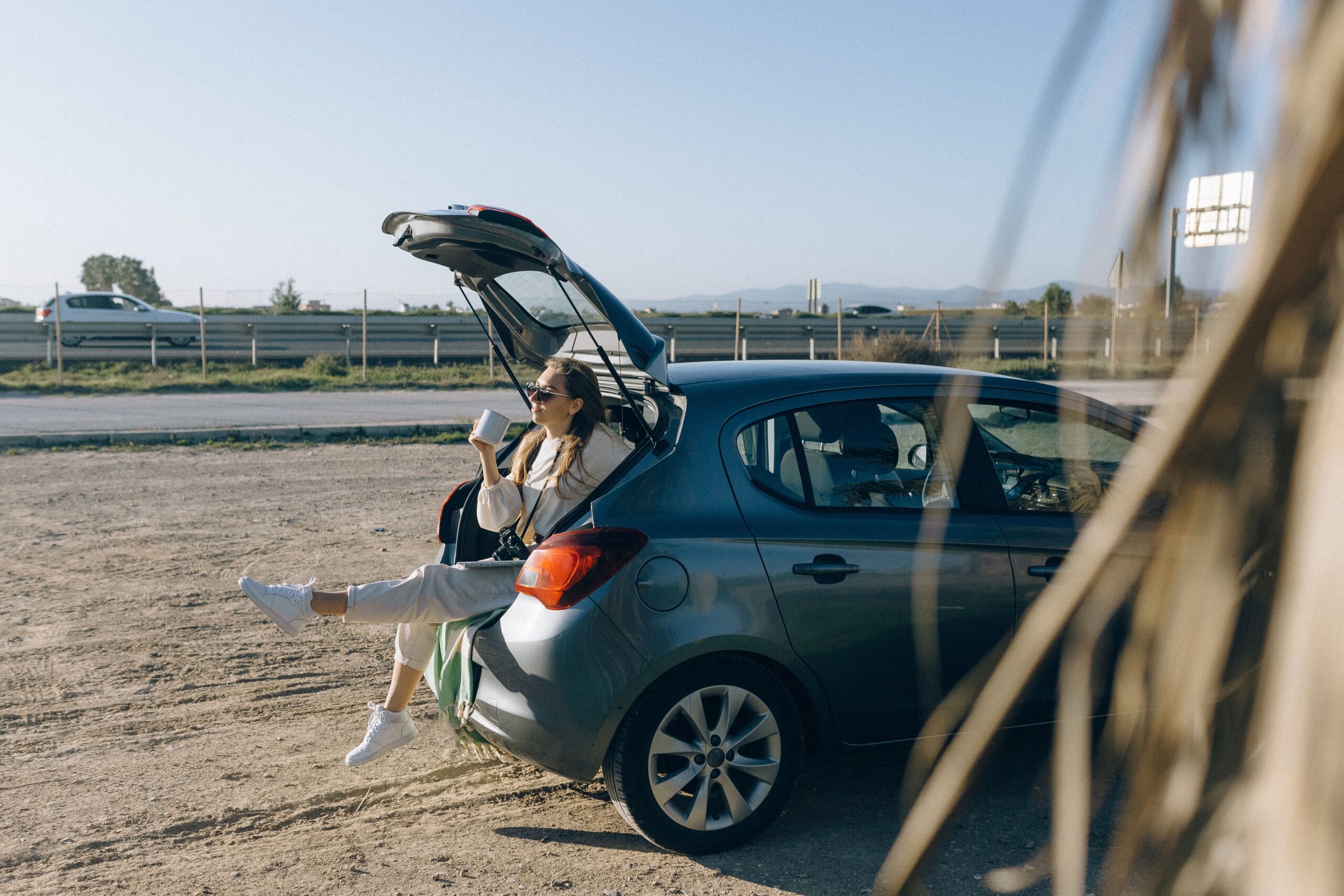 Woman relaxing beside an open rental car trunk